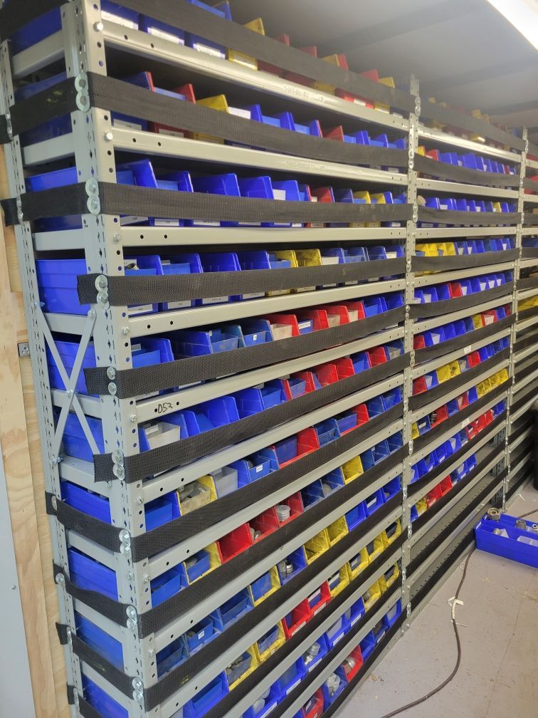 Shelves stacked with rows of blue, yellow, and red bins organized against a white wall.