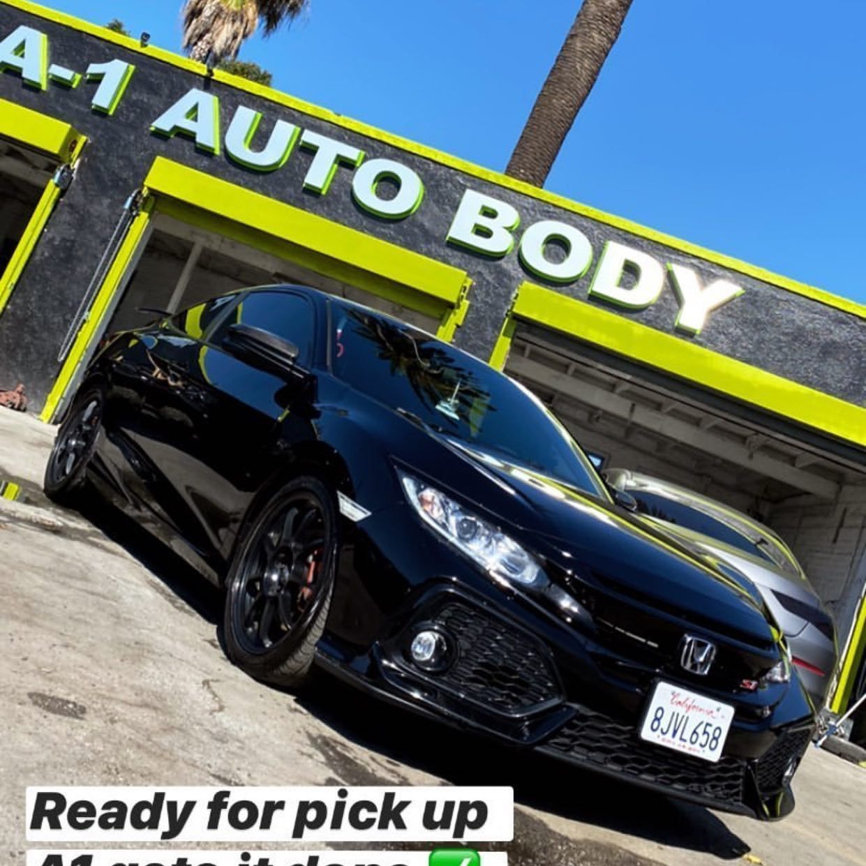A black car is parked in front of a 4- 1 auto body