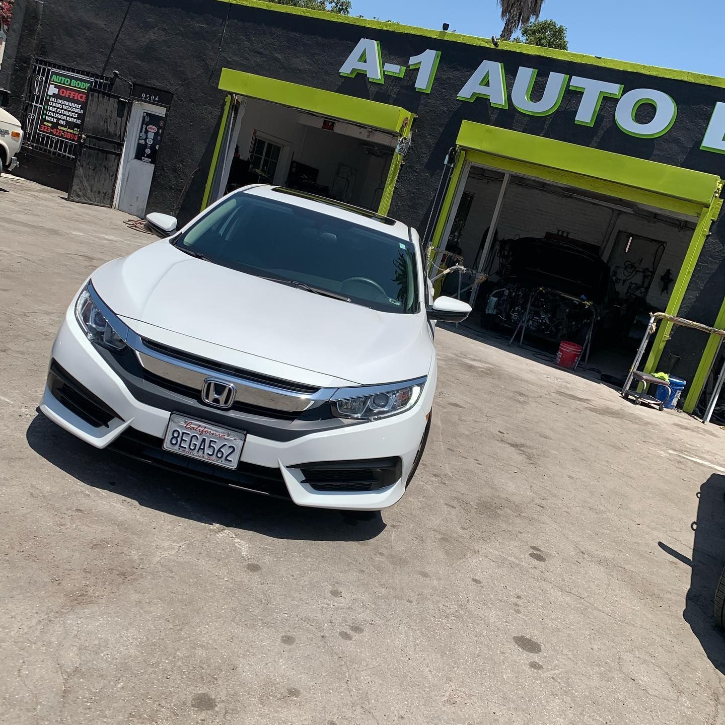 A white honda civic is parked in front of a a-1 auto repair shop
