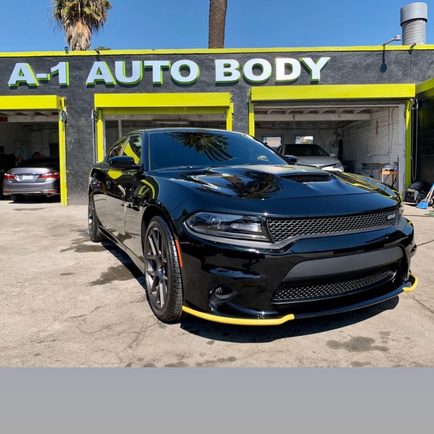 A black car is parked in front of a building that says a-1 auto body