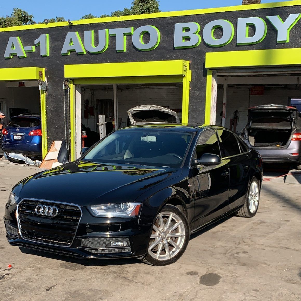 A black car is parked in front of a building that says a1 auto body.