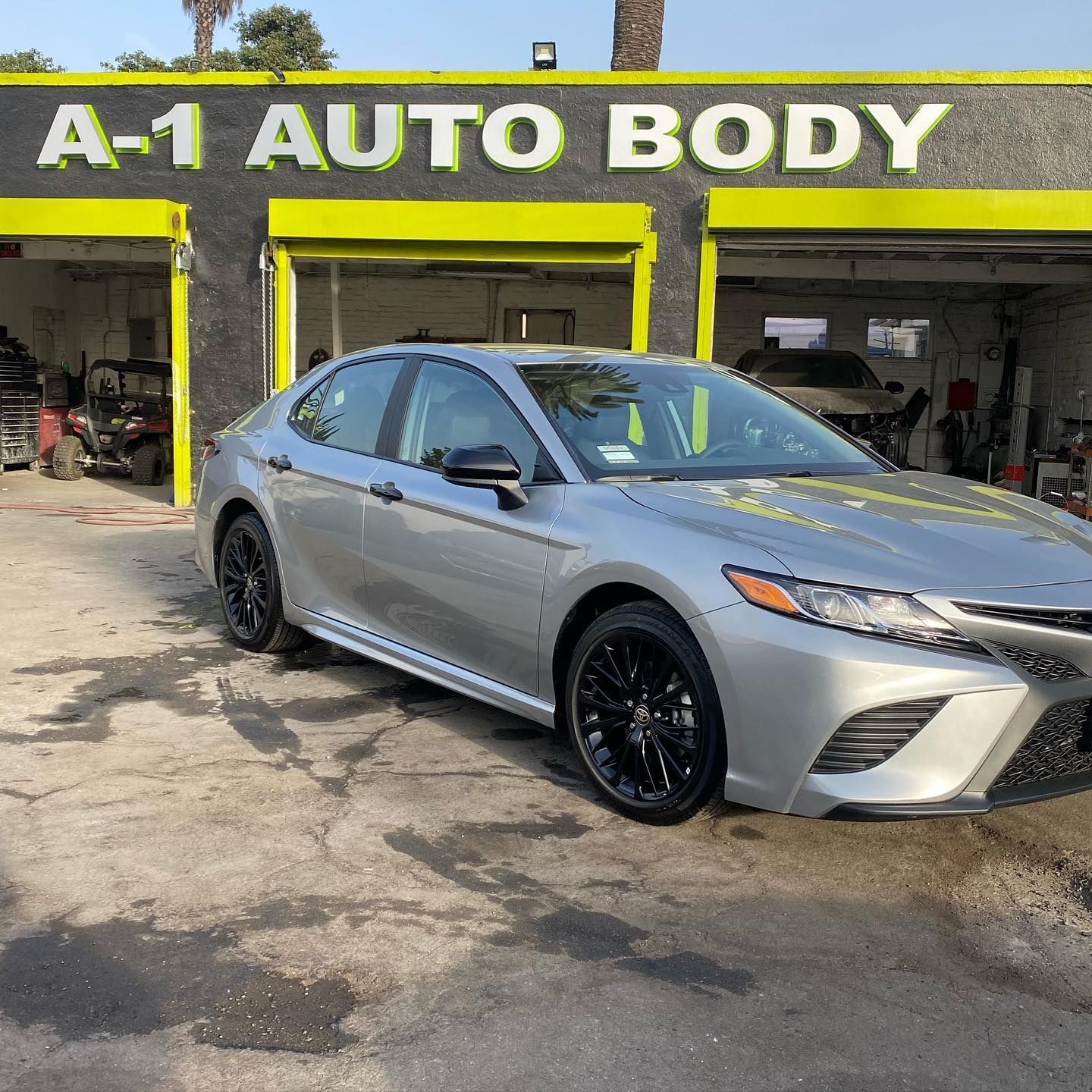 A silver car is parked in front of a building that says a-1 auto body