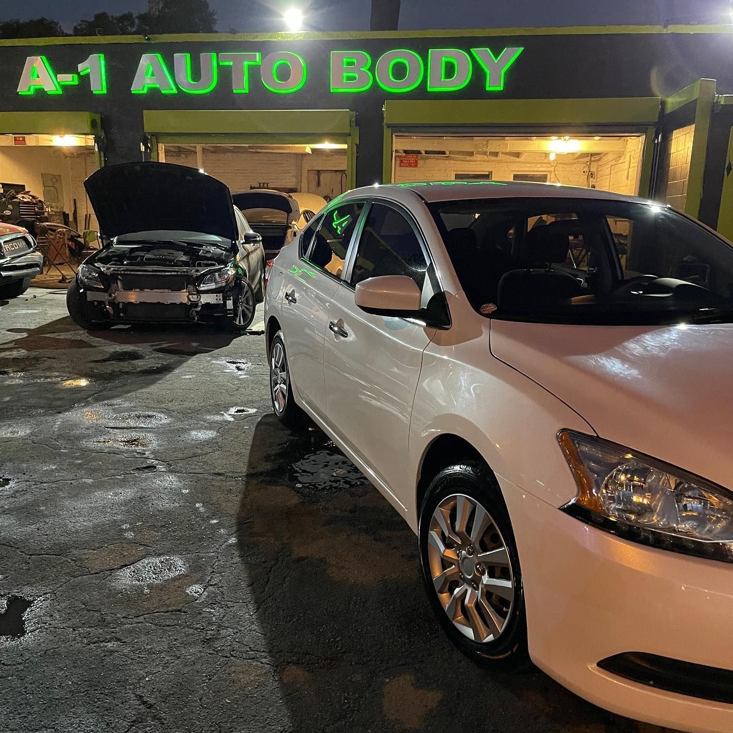 A white car is parked in front of a building that says a-1 auto body