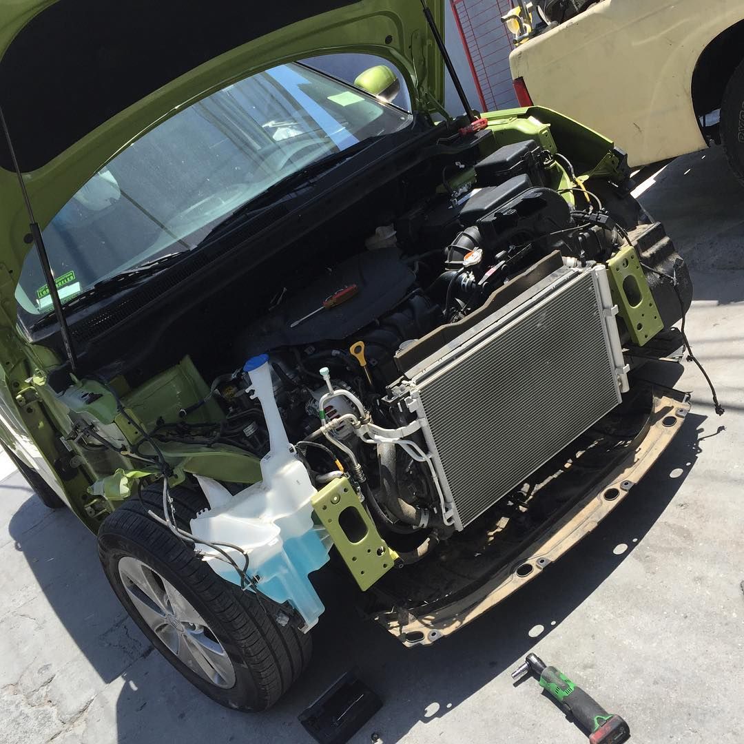 A green car with the hood up is being worked on