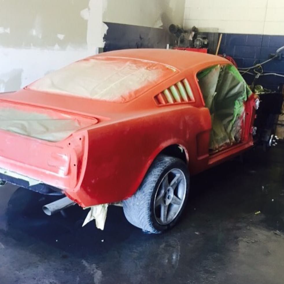 A red mustang is being painted in a garage