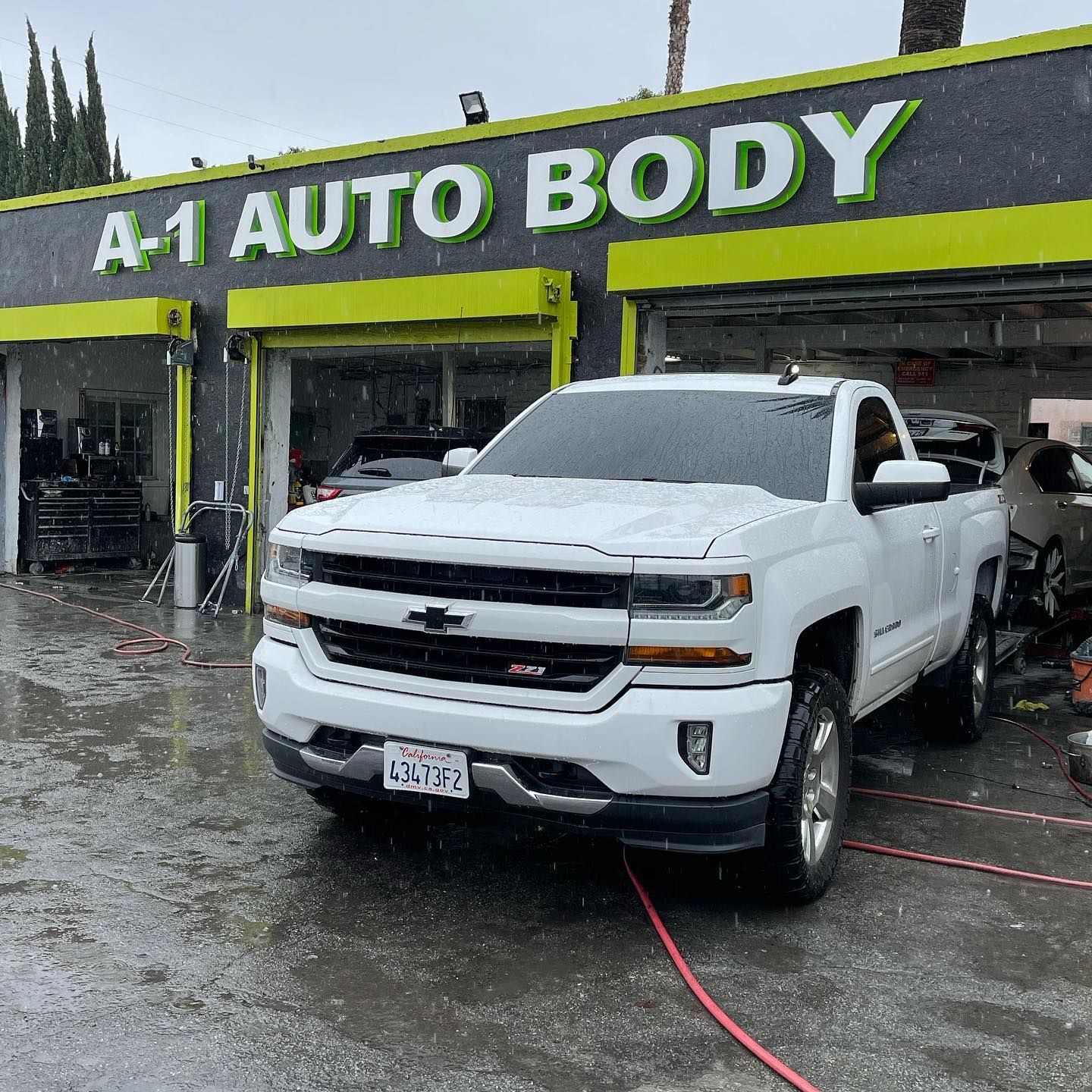 A white truck is parked in front of a car body shop.