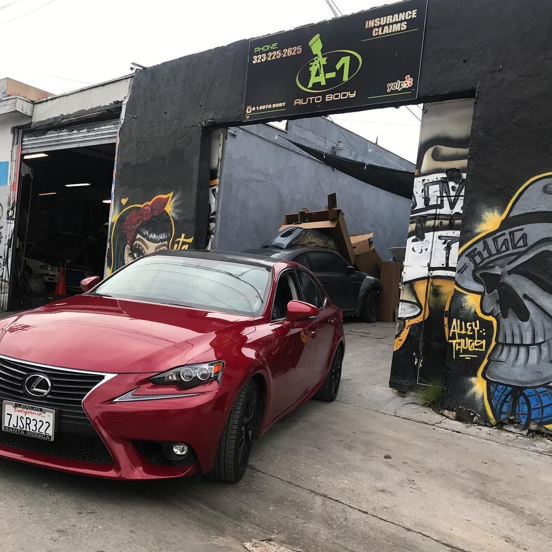 A red car is parked in front of a building with graffiti on it.