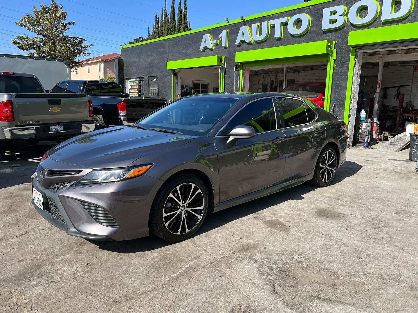 A gray car is parked in front of a green and black building.