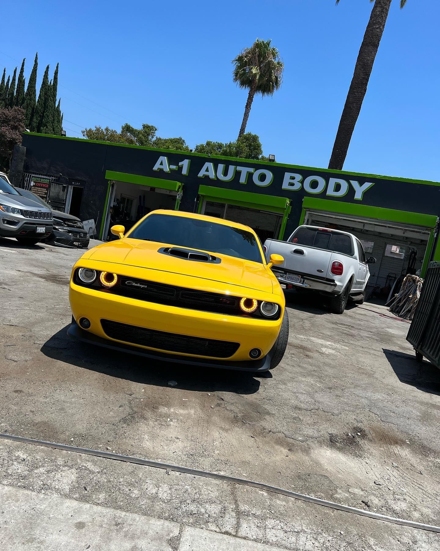 A yellow dodge challenger is parked in front of a car body shop.