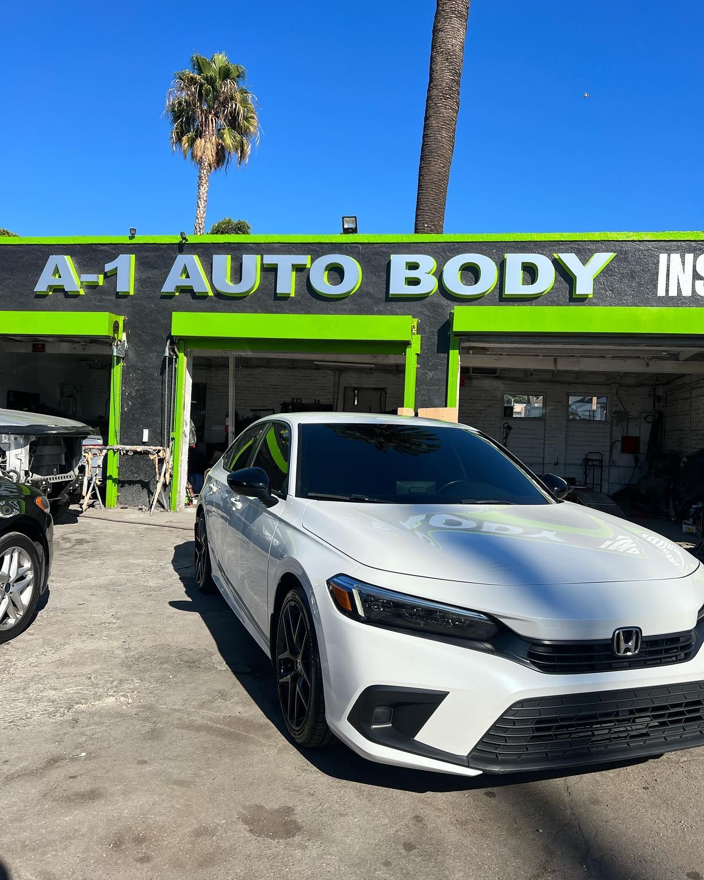 A white car is parked in front of a green and black building.