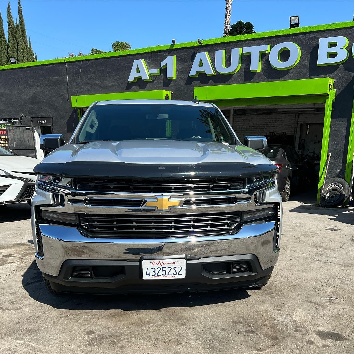 A silver truck is parked in front of a green and black building.