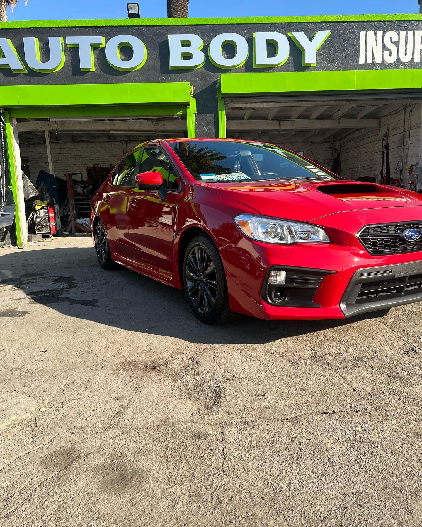 A red car is parked in front of an auto body shop.