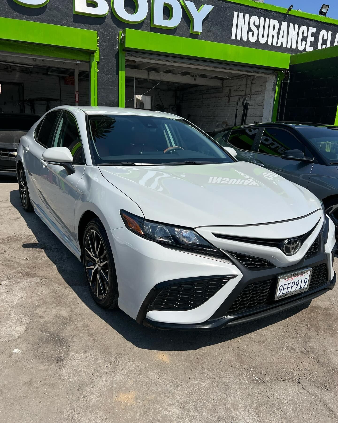A white car is parked in front of a body insurance company.