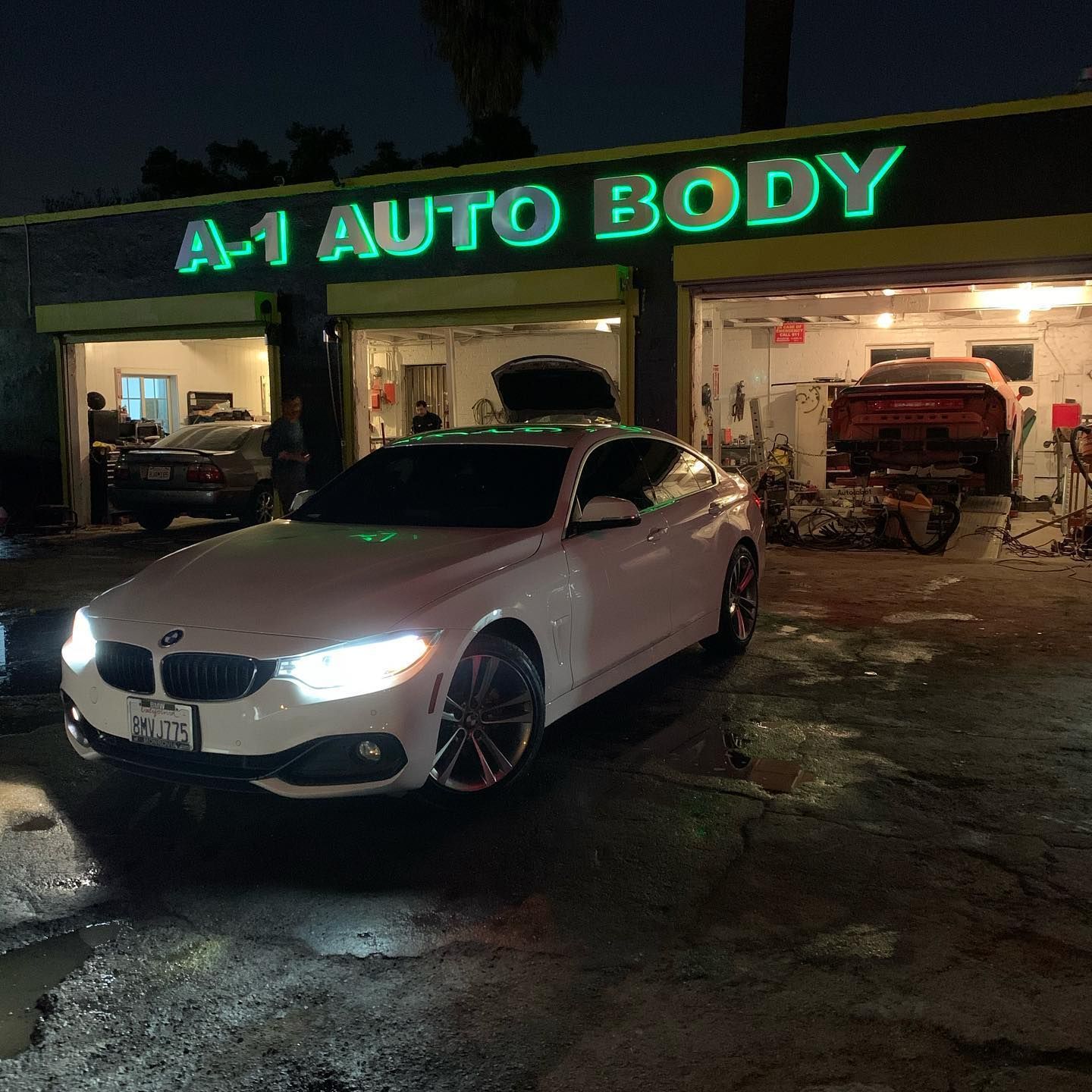 A white car is parked in front of a a-1 auto body