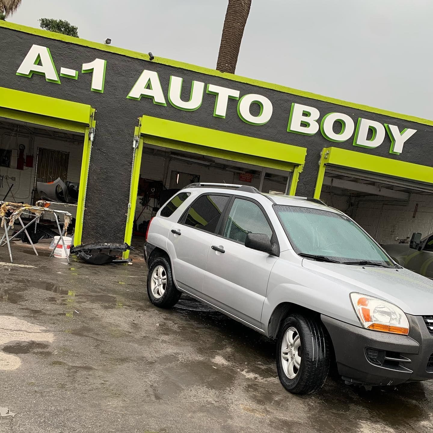A silver car is parked in front of a building that says a-1 auto body