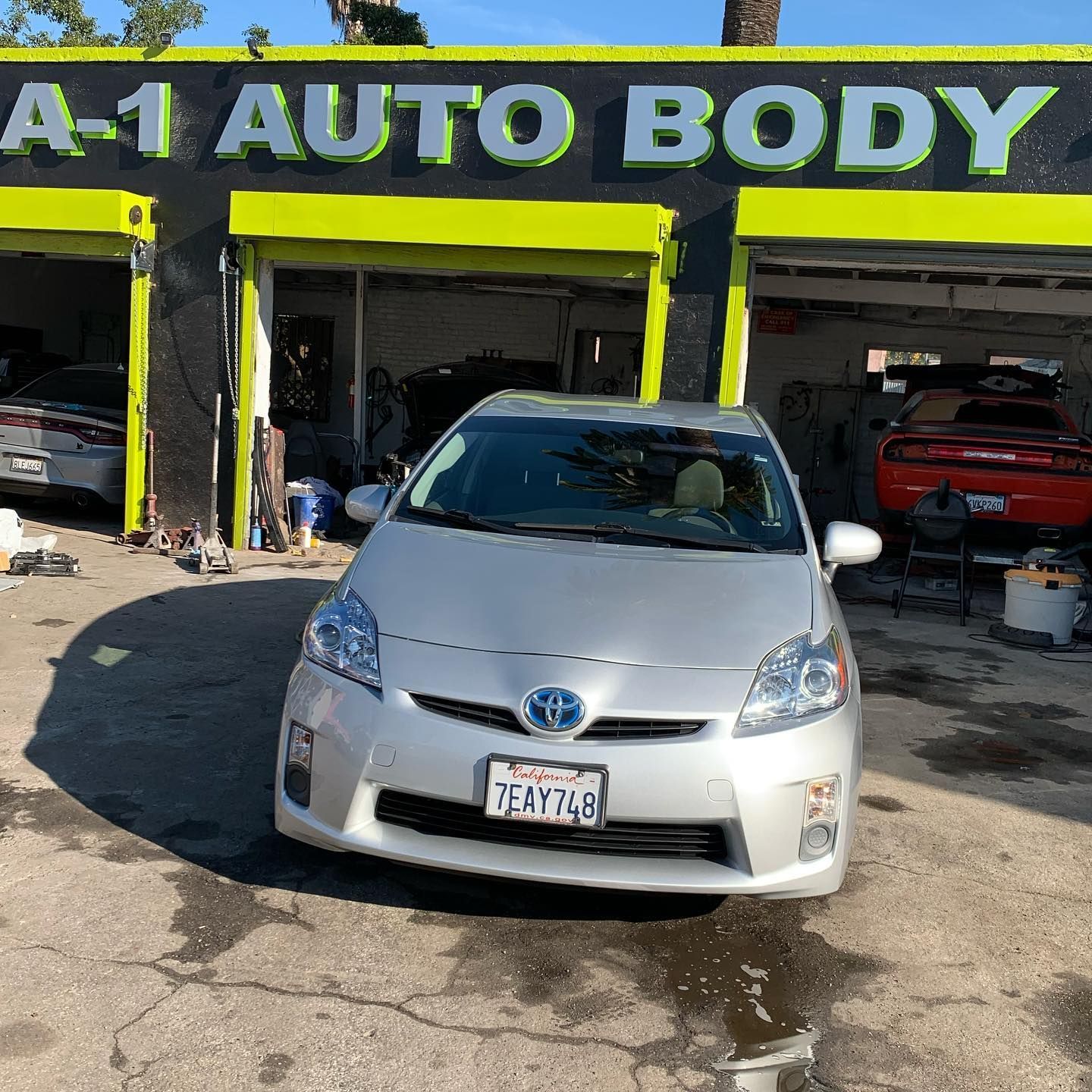 A silver car is parked in front of a building that says a-1 auto body.