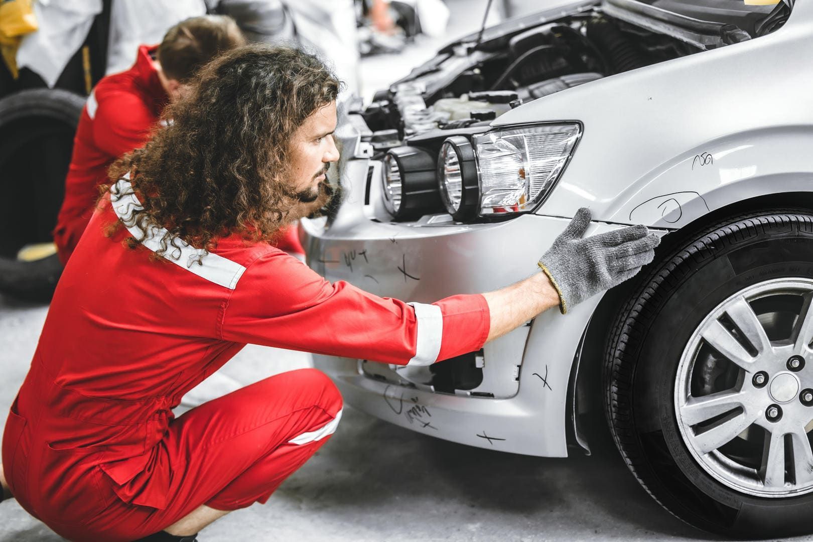 A man in a red jumpsuit is working on a car in a garage.