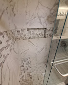 Marble-tiled shower with a mosaic accent and built-in shelf; glass door on the right.