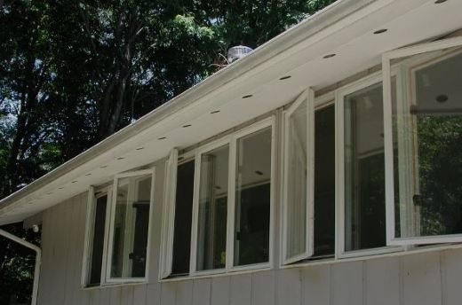 Row of white-framed casement windows, some open, on a light-colored building with a white overhang.