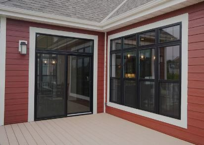Red exterior corner with black-framed windows and a sliding glass door. Cream-colored deck.
