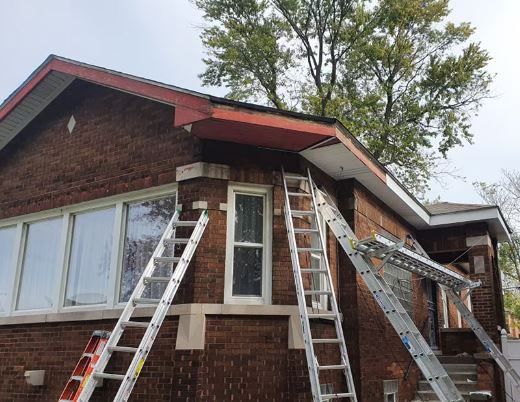 Brick house exterior with multiple ladders leaning against it; workers may be doing roof repairs.