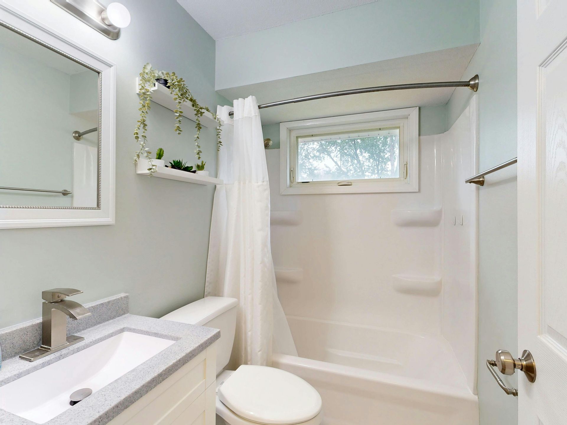 Bathroom with a white sink, toilet, and bathtub. Light blue walls, white trim, and a small window.