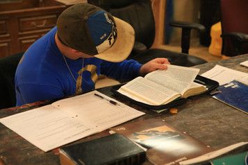 A man is sitting at a table reading a bible.