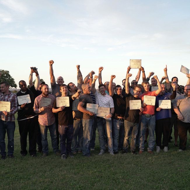 A large group of men are standing in a field holding up their fists and certificates