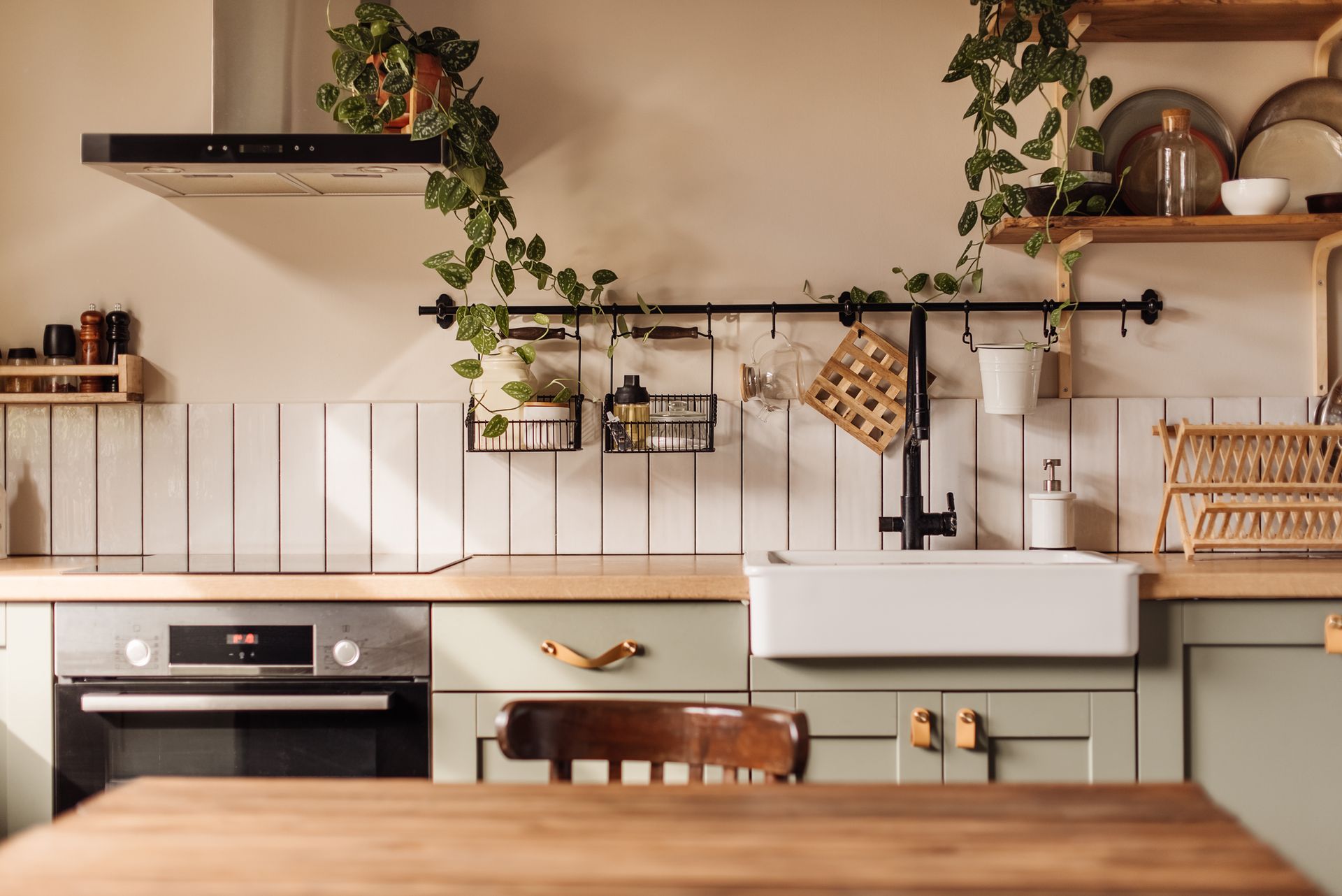 A kitchen with green cabinets, a white sink, a stove, and a wooden table.