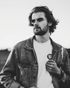 A man with a beard is wearing a denim jacket and a white shirt