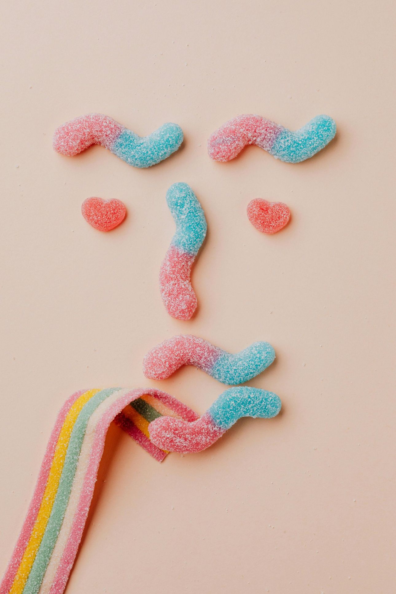 A face made out of gummy worms on a pink background.