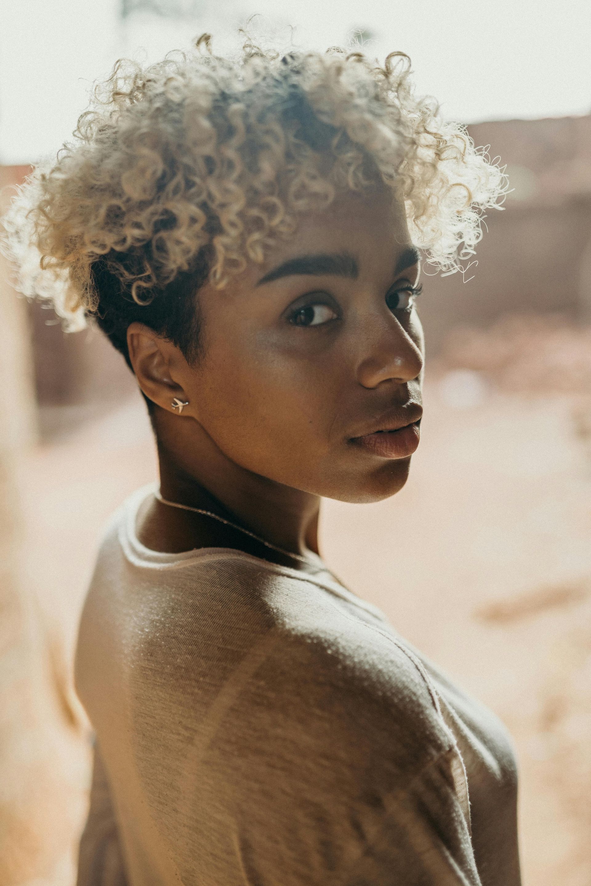 A woman with blonde curly hair is looking over her shoulder at the camera.