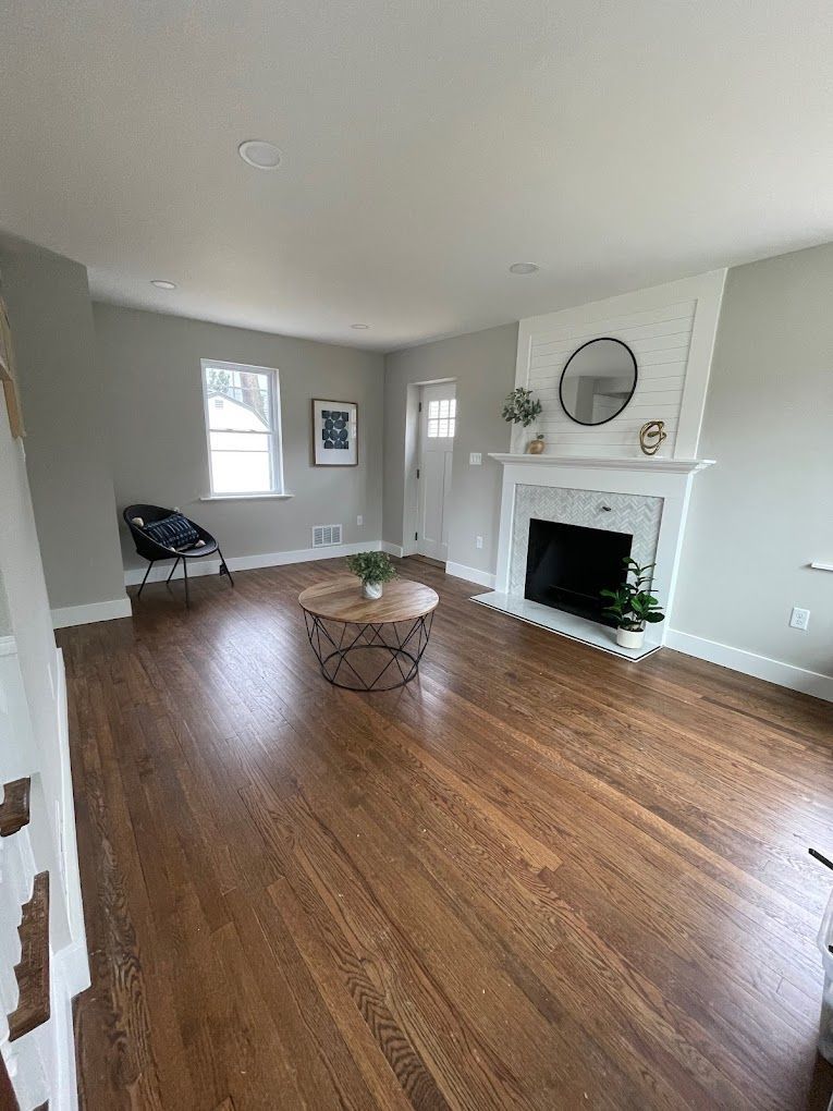 Empty living room with wood floors, fireplace, and light gray walls.