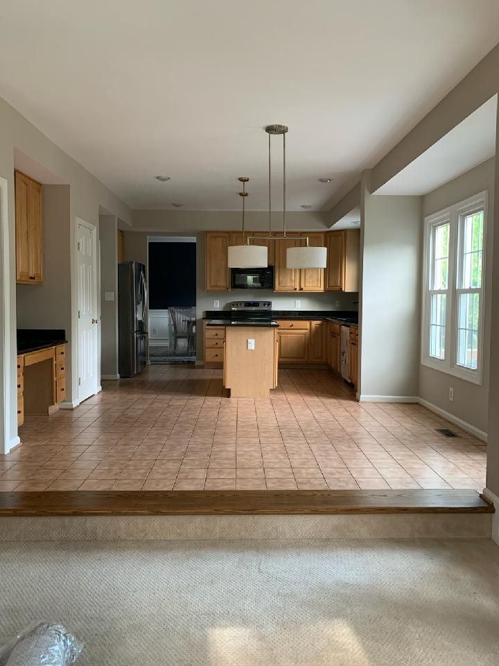 Open floor plan: kitchen with wood cabinets, center island, and tiled floor, adjacent to a living area with a carpeted floor.