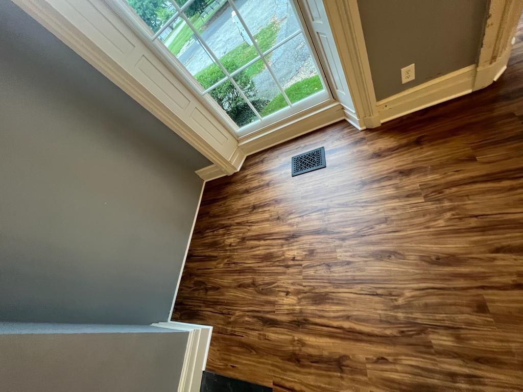 Wood-look flooring in a room with a window and gray walls. Air vent in floor.
