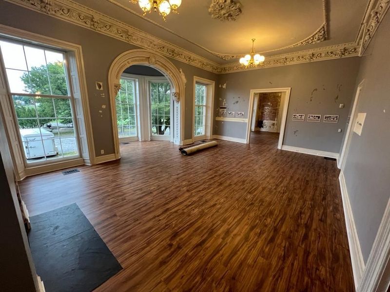 Spacious room with wood floor, large windows, and ornate ceiling details.