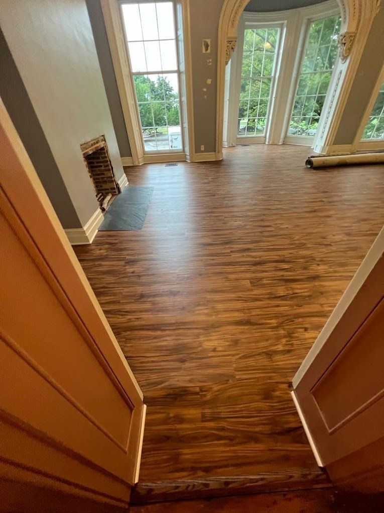 Dark wooden flooring in a room with large windows, fireplace, and ornate white trim.