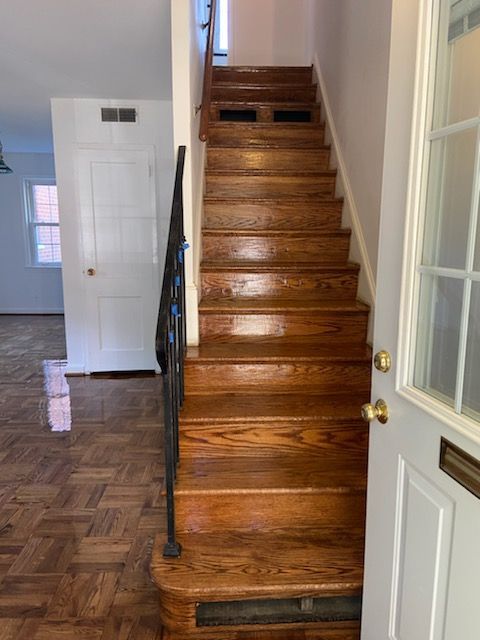 Wooden staircase in a home's entryway, leading upwards. Open white door on right, doorway to the left.