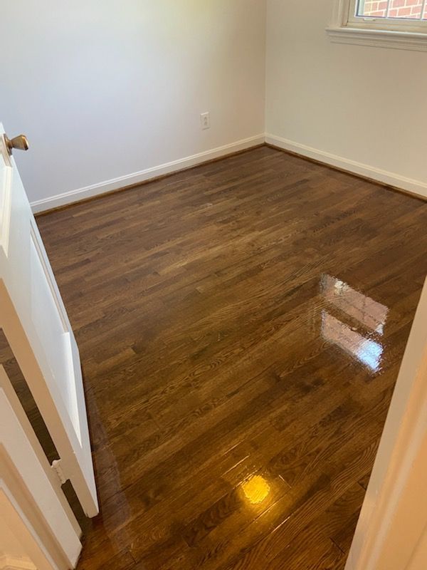 Empty room with newly refinished, shiny, dark wood floors and white walls.
