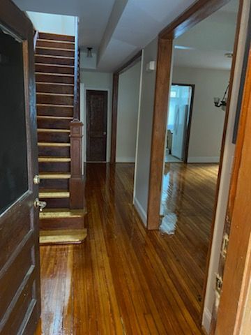 Wooden-floored entry hall with staircase and doorways. Dark wood door on the left, open to the space.