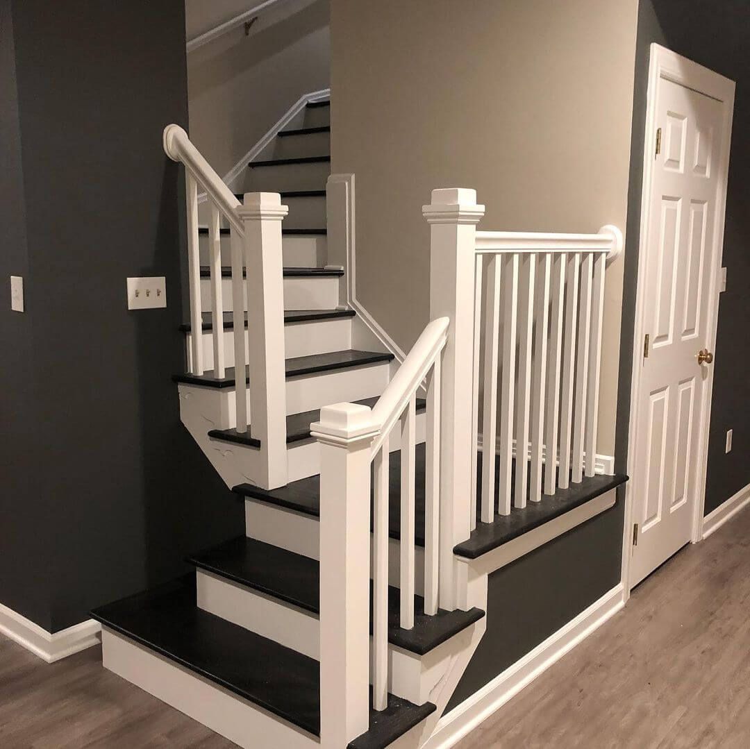 Staircase with white railing, black treads, and dark gray wall, next to a white door.
