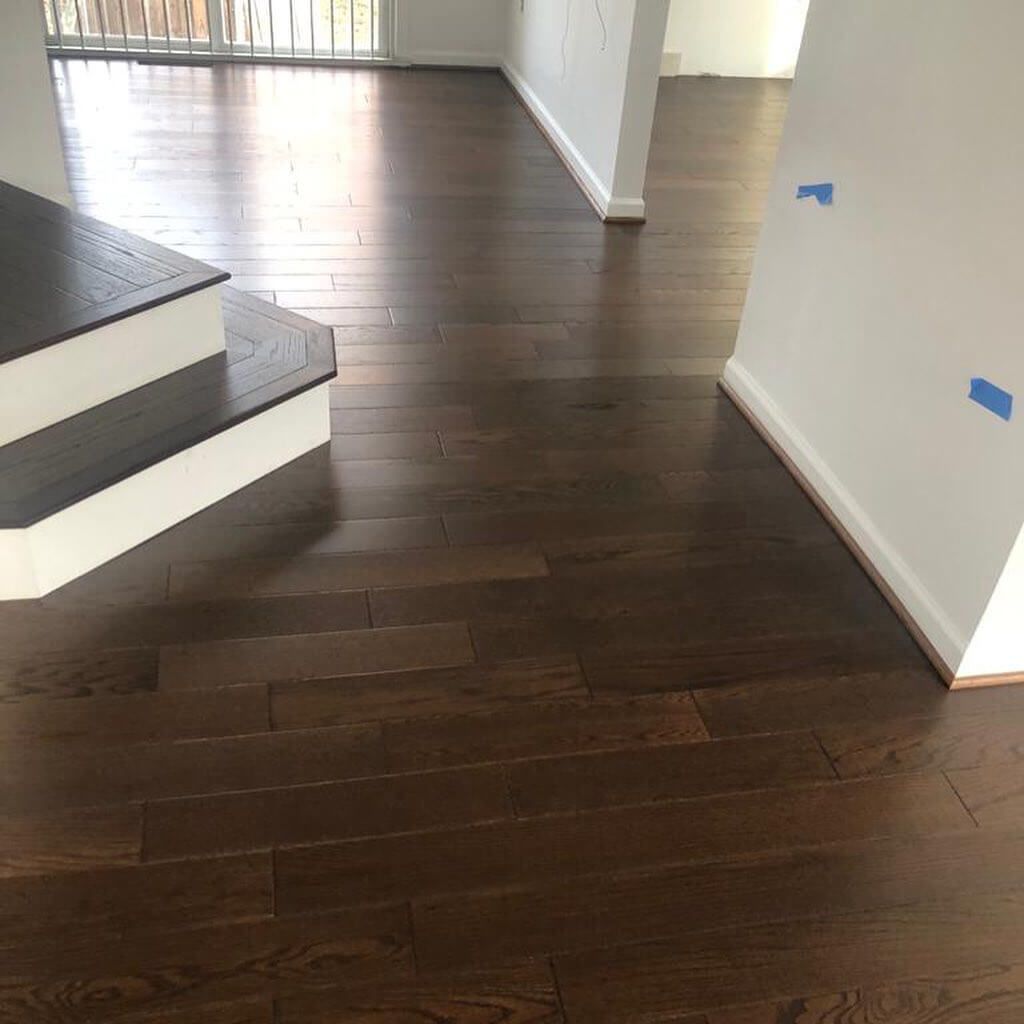Dark stained hardwood floor in a home, next to a staircase and white walls.