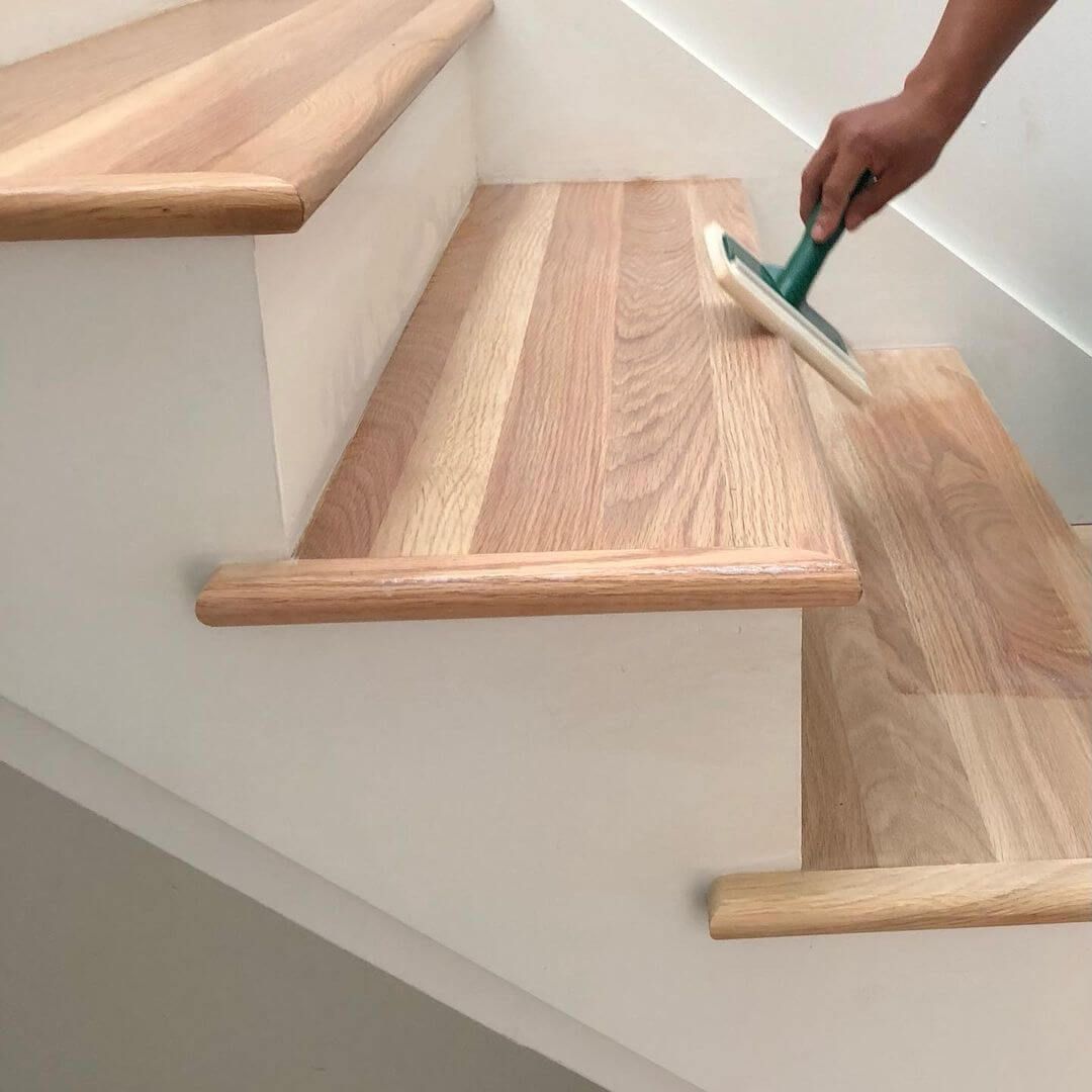 Person applying finish to wooden staircase treads.