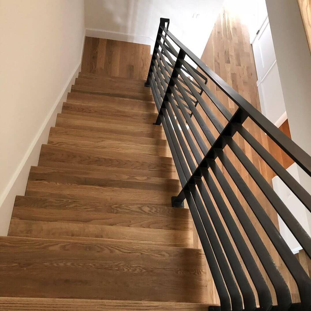 Wooden staircase with black metal railing, viewed from above.