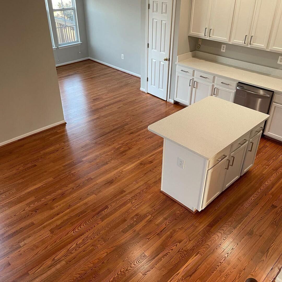 Hardwood floors in a kitchen with white cabinets, island, and stainless steel dishwasher.