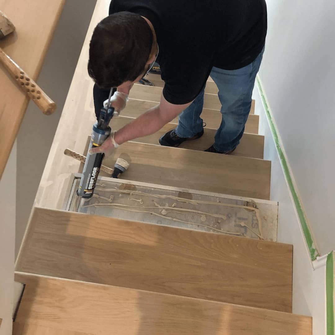 Person installs wood flooring on stairs, using tools.