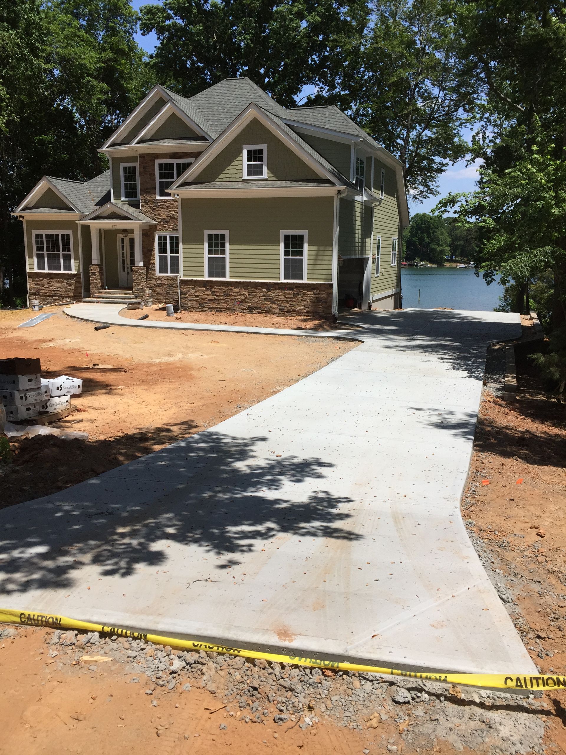 A two-story green suburban house with stone accents and a newly poured concrete driveway under construction.