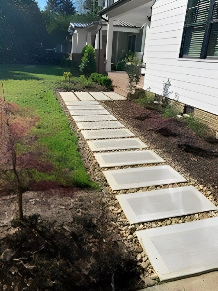 A concrete paver walkway leading to a house entrance, bordered by grass on one side and a garden bed with mulch on the other.