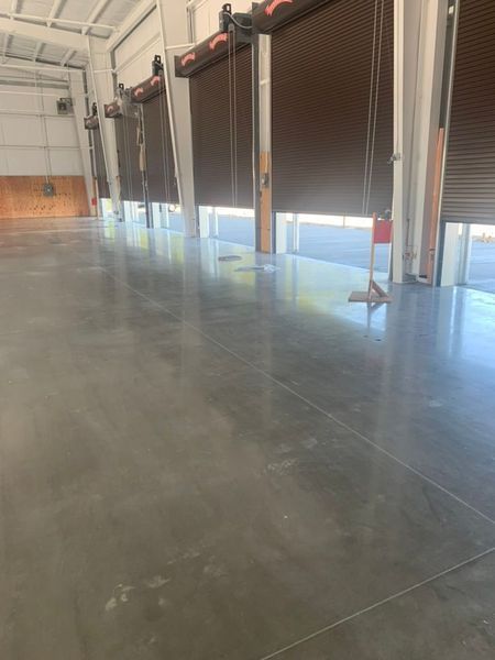 An interior view of a warehouse with a polished concrete floor, light-colored walls, and several roll-up bay doors.