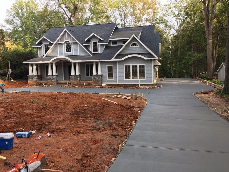 A two-story grey craftsman house with a porch and a newly poured concrete driveway surrounded by red dirt construction.